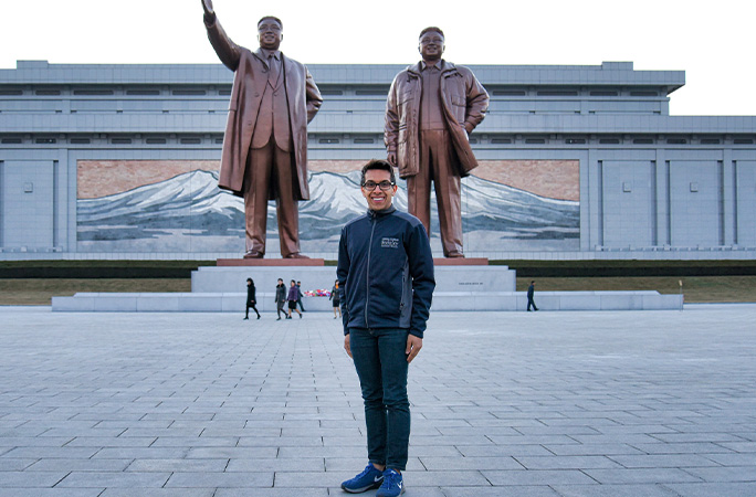 Indy standing in front of two large statues in North Korea