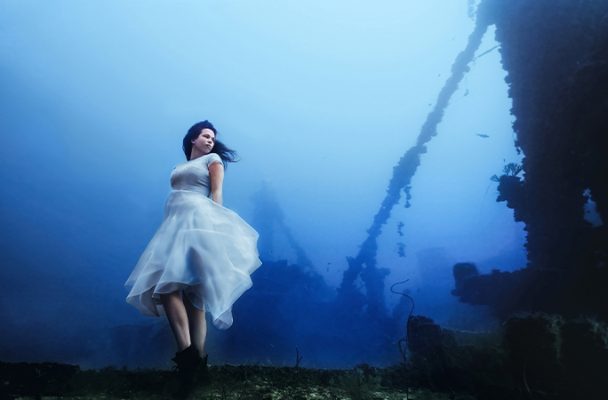 Model posing underwater with a shipwreck