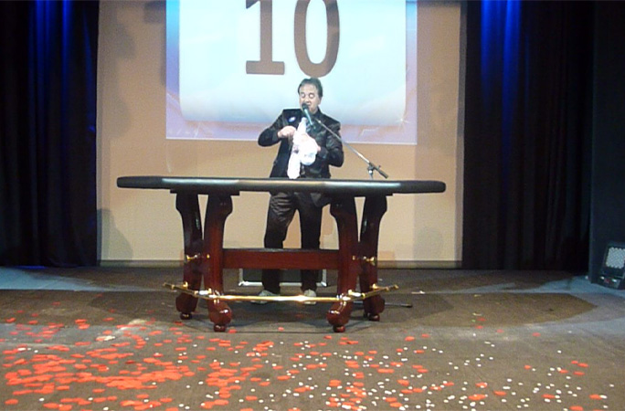 A magician performs under a backdrop with his number