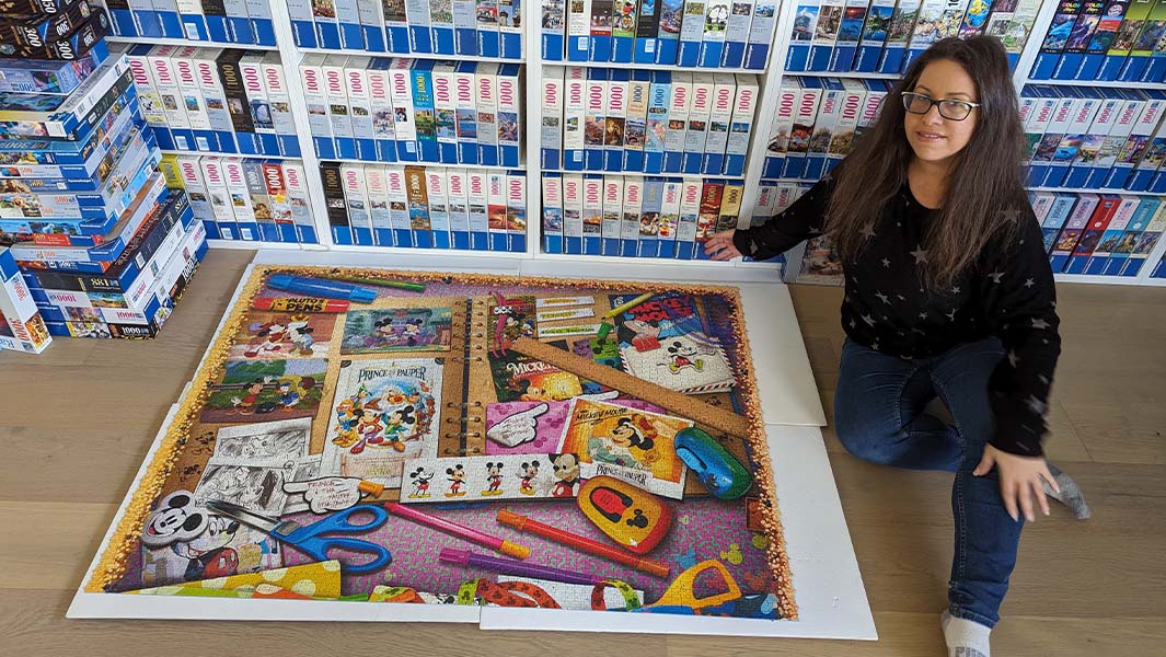 Liza with a completed puzzle and shelves full of other jigsaws