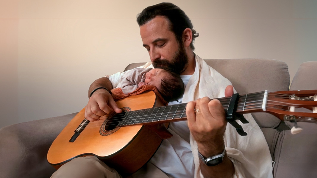 Philip playing his guitar with baby William laying on top