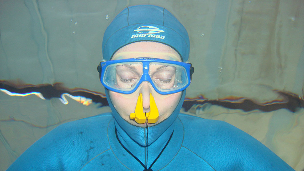 split header of a woman underwater holding her breath and a man above water with stopwatches held up in front of him