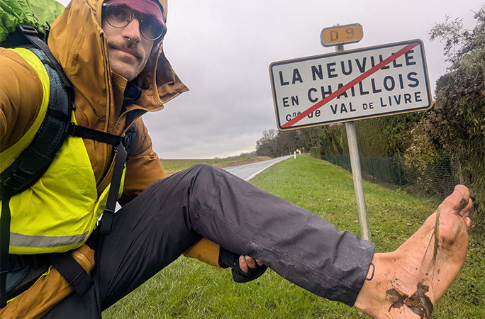 Eamonn holding up his dirty foot in front of a road sign