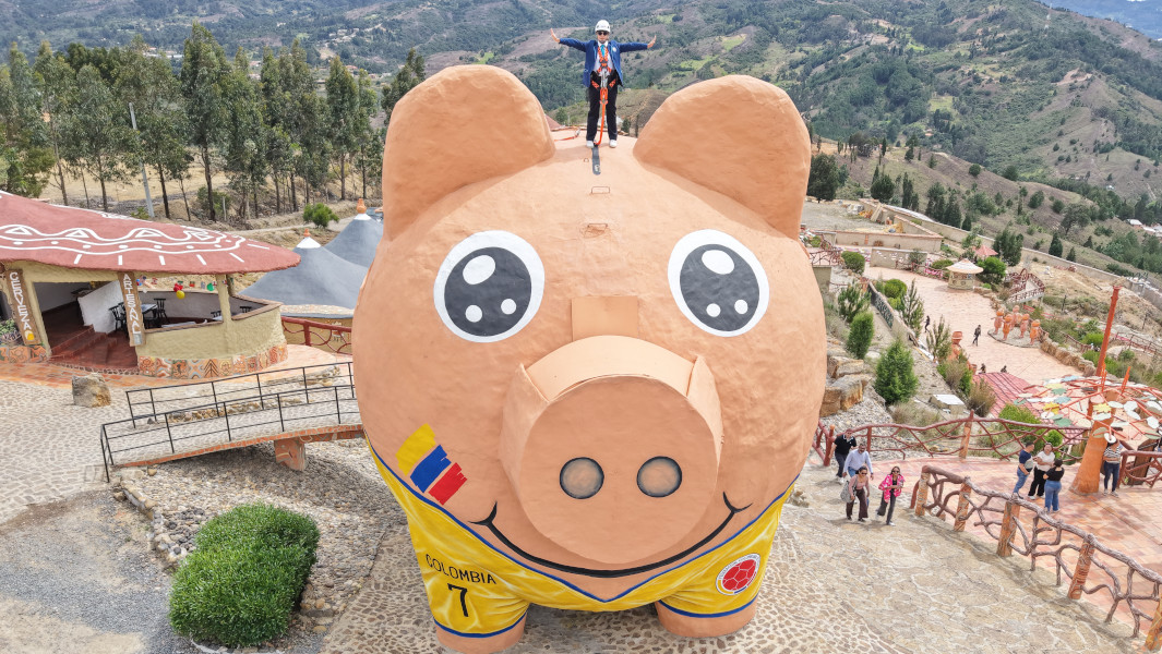 A woman standing on the largest piggy bank while people stand below